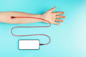 The hand is connected by a red power cord to a smartphone with free space on a blue background. photo