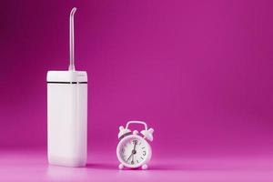 An irrigator for brushing teeth on a pink background with a clock. photo