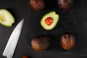 aguacates maduros en una cesta sobre una mesa negra, con una fruta cortada y una piedra. foto