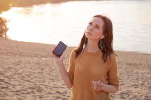 mujer con auriculares blancos relajándose en el lago y escuchando música al atardecer. foto