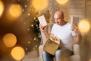 hombre feliz en silla en el fondo del árbol de navidad con un regalo en sus manos foto