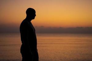 Male silhouette on background sea at sunset looks to side alone. Man enjoying photo