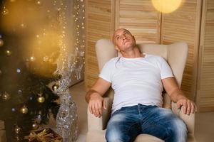 hombre pensativo sentado en una silla cerca del árbol de navidad foto