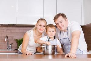 amables padres caucásicos enseñando a su pequeño y adorable hijo a cocinar sano foto