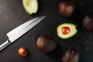 Sliced and whole organic avocado Hass with a knife on a black background. photo