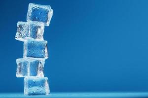 cubos de hielo con torre de gotas de agua en una fila sobre un fondo azul. foto