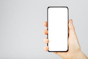 Hand holds black smartphone with blank white screen and modern frameless design isolated on gray background. photo