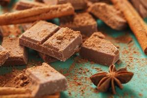 Chocolate broken into slices with cocoa powder and spices on a green background