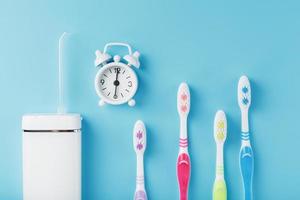 Oral irrigator and Toothbrushes in different colors with an alarm clock on a blue background. photo