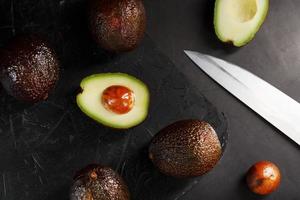 Sliced and whole organic avocado Hass with a knife on a black background. photo