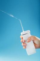 Irrigator in hand for cleaning the mouth with a shot of water jet on a blue background photo