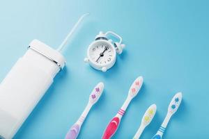 Oral irrigator and Toothbrushes in different colors with an alarm clock on a blue background. photo