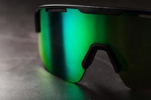 Sports glasses with a green mirrored lens and black frames on a black background photo