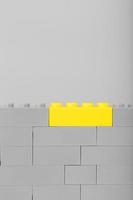 A gray wall made of a toy construction set with the last yellow brick photo