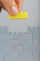 A gray wall made of a toy construction set with the last yellow brick in hand photo