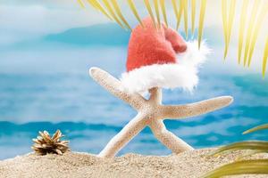 White starfish with Santa Claus's hat with cone on beach behind sea. Christmas, New Year card. Holiday in hot countries photo