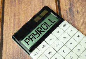 word payroll on calculator display and wooden background photo