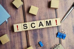 The word SCAM is written on wooden blocks on a wooden background photo