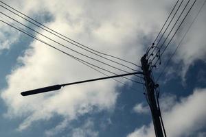 poste de electricidad moderno con linterna y cables de línea eléctrica. cielo azul y nubes como fondo. concepto de conocimiento de ingeniería moderna para transmisión de energía, conexión, comunicación e iluminación foto