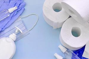 Set of important items for Covid-19 quarantine. Toilet paper, rubber disposable gloves with surgical face mask and hand sanitizer with liquid soap bottle on blue background photo