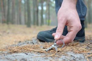 mano masculina recogiendo llaves perdidas de un suelo en el camino de madera de abeto de otoño. el concepto de encontrar algo valioso y buena suerte foto