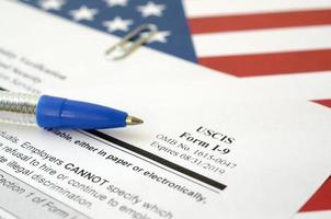 I-9 Employment Eligibility Verification blank form lies on United States flag with blue pen from Department of Homeland Security photo