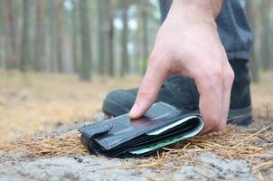 Male hand picking up lost wallet from a ground in autumn fir wood path. The concept of finding a valuable thing and good luck photo