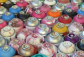 Large number of used colorful spray cans of aerosol paint lying on the treated wooden surface in the artist's graffiti workshop close up. Dirty and stained cans for art photo