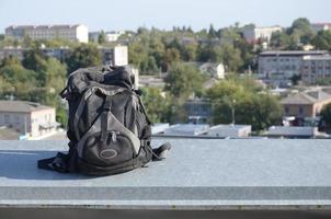 Black backpack lies on metal border of residental multistorey building rooftop in sunny weather photo