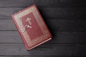 Silver necklace with crucifix cross on christian holy bible book on black wooden table. Asking blessings from God with the power of holiness, which brings luck photo