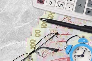 100 Ukrainian hryvnias bills and calculator with glasses and pen. Business loan or tax payment season concept. Time to pay taxes photo