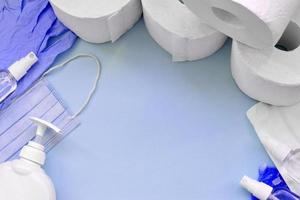 Set of important items for Covid-19 quarantine. Toilet paper, rubber disposable gloves with surgical face mask and hand sanitizer with liquid soap bottle on blue background photo