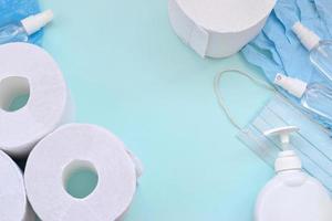 Set of important items for Covid-19 quarantine. Toilet paper, rubber disposable gloves with surgical face mask and hand sanitizer with liquid soap bottle on blue background photo