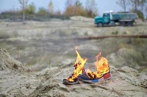 Burning sports sneakers or gym shoes on fire stand on sandy beach coast. Athlete burned out. Physical exertion during training concept photo