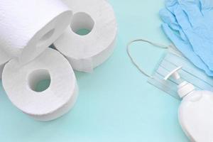 Set of important items for Covid-19 quarantine times. Toilet paper, rubber disposable gloves with surgical face mask and liquid soap bottle on blue background photo