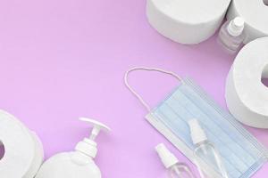 Set of important items for Covid-19 quarantine times. Toilet paper with surgical face mask and hand sanitizer with liquid soap bottle on lilac background photo