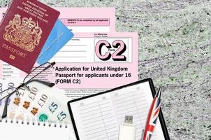 English form C2 Application for United Kingdom passport for applicants under 16 lies on table with office items. UK passport paperwork photo