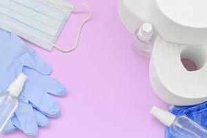 Set of important items for Covid-19 quarantine. Toilet paper, rubber disposable gloves with surgical face mask and hand sanitizer on lilac background photo