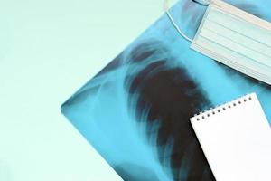 Respiratory mask and empty notepad page on x-ray of human lungs, top view. Coronavirus Covid-19 disease concept. photo