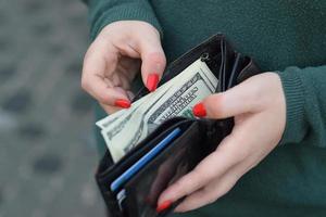 Woman hands with red nails holds black mens purse with many US hundred dollars bills. Concept of salary earnings or counting money photo
