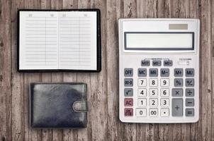 Office flat lay composition with calculator, address book and black purse on brown wooden table background with top view. Accountant paperwork concept photo