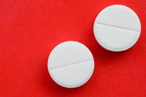 A few white tablets lie on a bright red background surface. Background image on medical and pharmaceutical topics photo