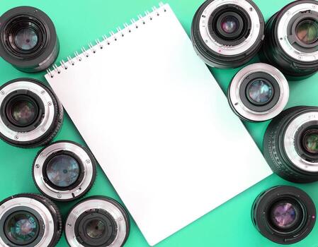 Several photographic lenses and white notebook lie on a bright turquoise background. Copy space photo