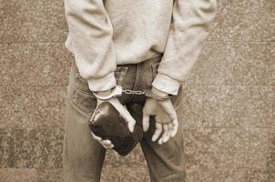 Arrested drug dealer in police handcuffs with big heroin drug package on dark wall background photo