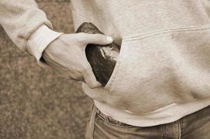 Traficante de drogas sacando una bolsa con cocaína del bolsillo de la sudadera con capucha sobre fondo de azulejos oscuros de cerca foto