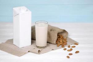 vaso de leche de almendras con nueces de almendras sobre tela de lona sobre mesa de madera blanca. leche alternativa láctea para desintoxicación, alimentación saludable y dietas foto