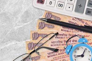 Billetes de 10 rupias indias y calculadora con gafas y bolígrafo. préstamo comercial o concepto de temporada de pago de impuestos. hora de pagar impuestos foto