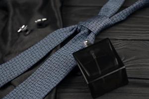 A bottle of mens cologne and cufflinks with blue tie lie on a black luxury fabric background on a wooden table. Mens accessories photo