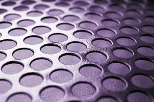 Black metal computer case panel mesh with holes on purple background. Abstract close up photo