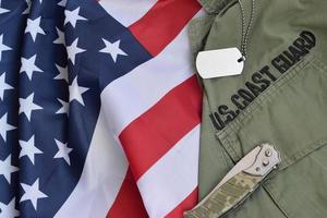 Military dog tag token and knife lies on Old US Coast Guard uniform and folded United States Flag photo